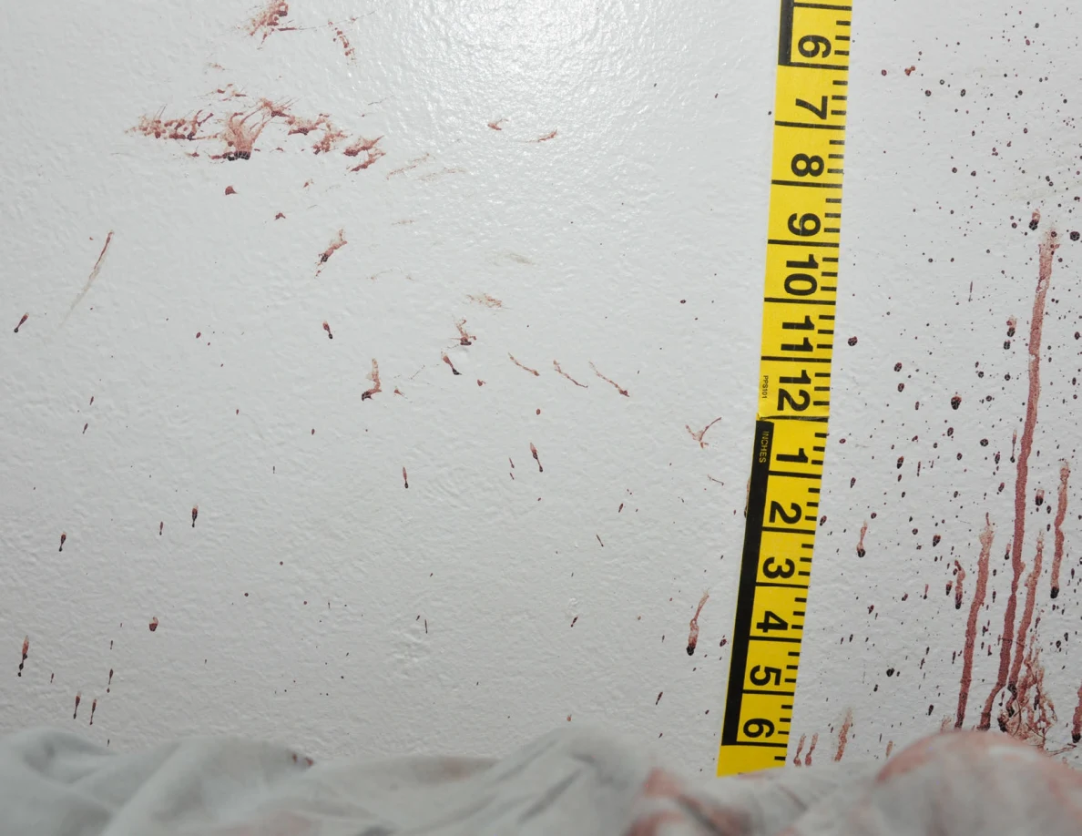 Reddish wall smears and streaks beside vertical yellow measuring tape.