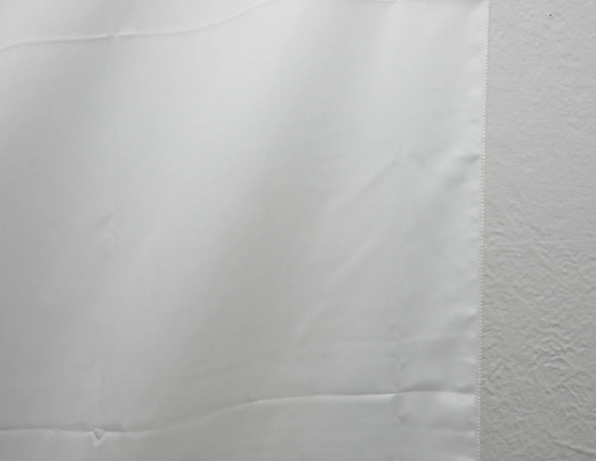 Close view of the edge of a white fabric wall hanging.