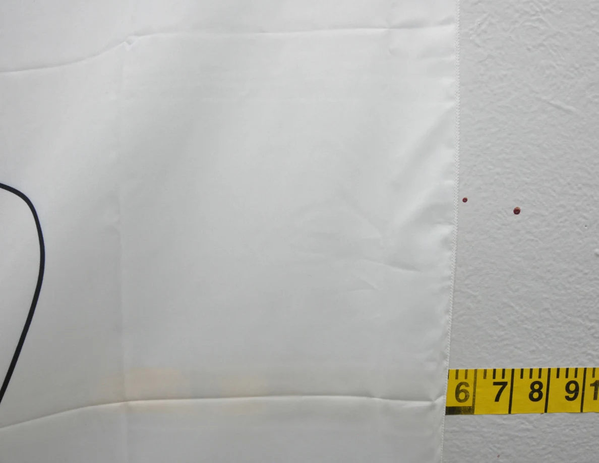 Fabric wall hanging beside reddish spots and yellow measuring tape.