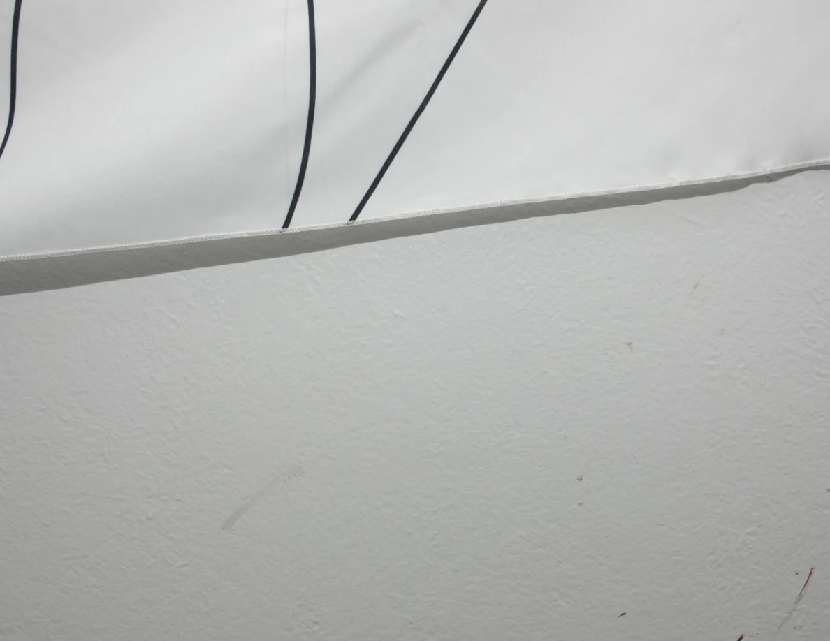 Lower edge of a fabric hanging beside faint marks on a white wall.