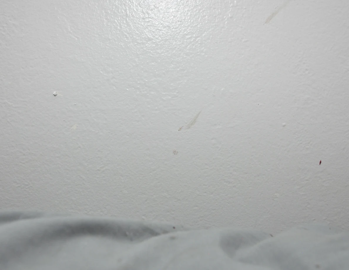 Faint streaks on a pale wall above a sheet.