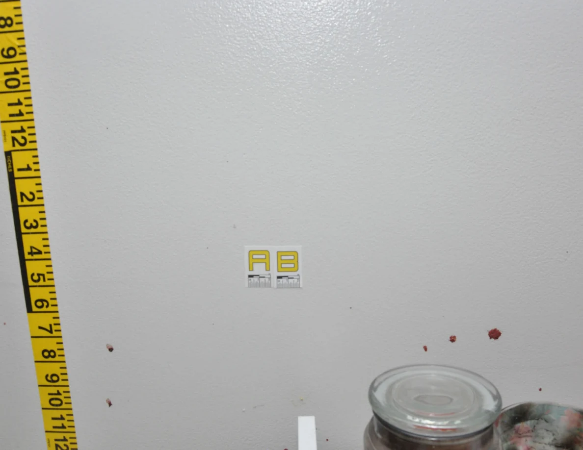 Wall label AB beside measuring tape above candles.