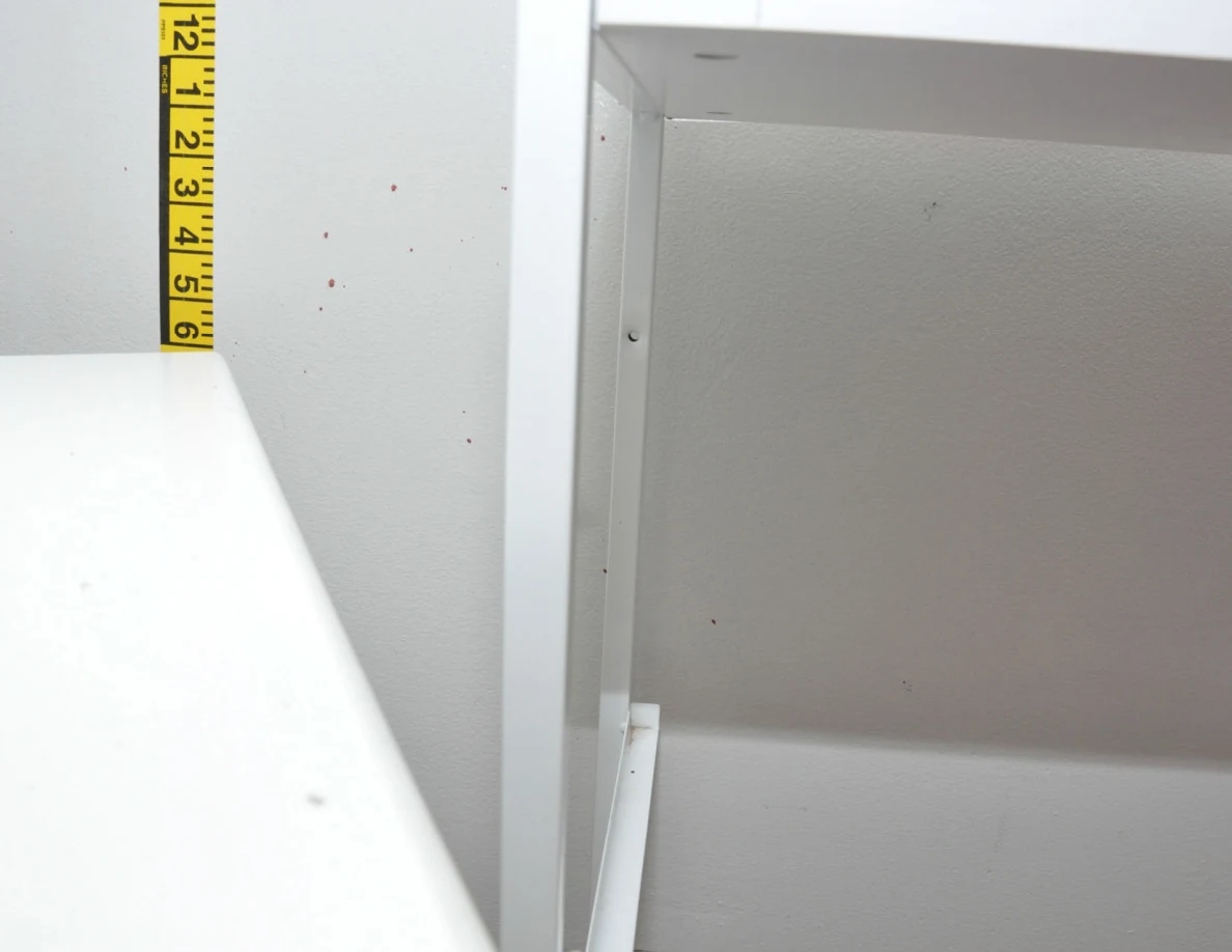 Wall spots and measuring tape below a cabinet edge.