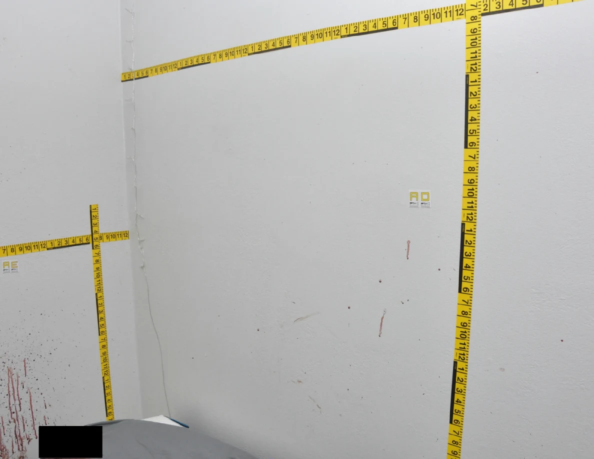 Wall corner with reddish streaks, label AD and horizontal and vertical yellow measuring tapes.