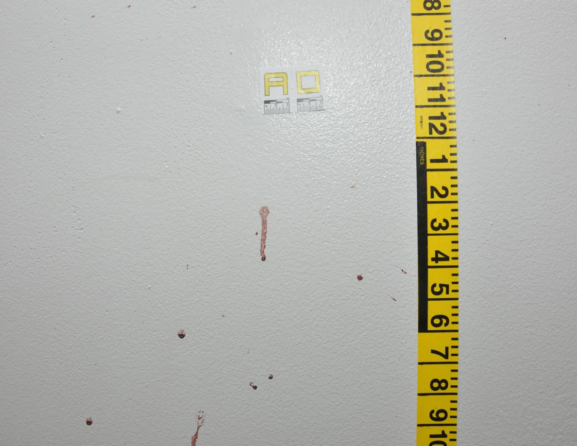 Reddish wall drops and streaks beside label AD and vertical yellow measuring tape.