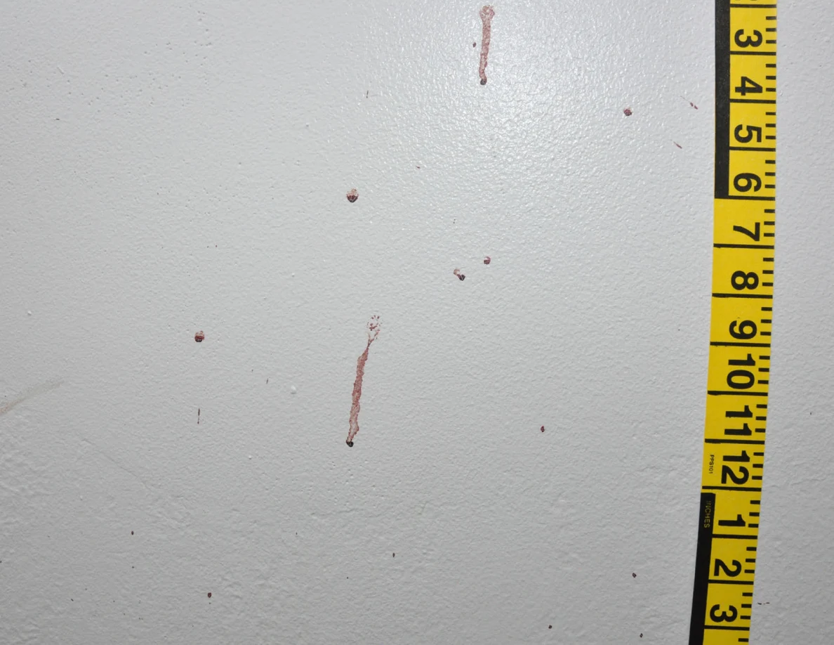 Close view of reddish wall drops and streaks beside vertical yellow measuring tape.