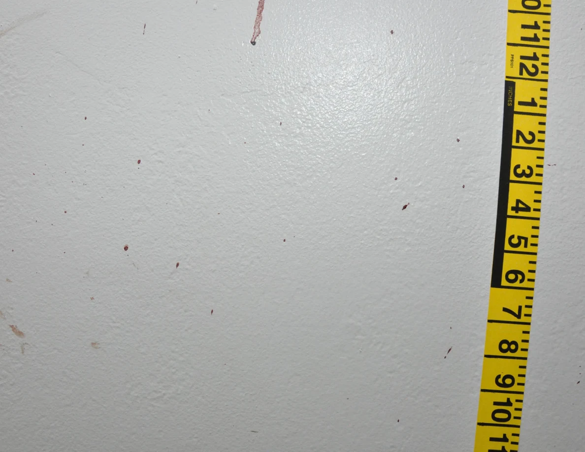 Reddish spots and a streak on a white wall beside vertical yellow measuring tape.