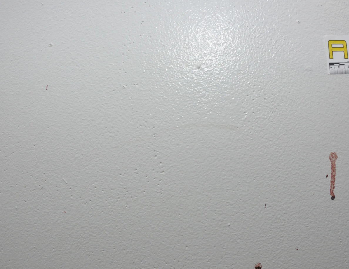 Reddish streak on a white wall beside a partially visible letter label.