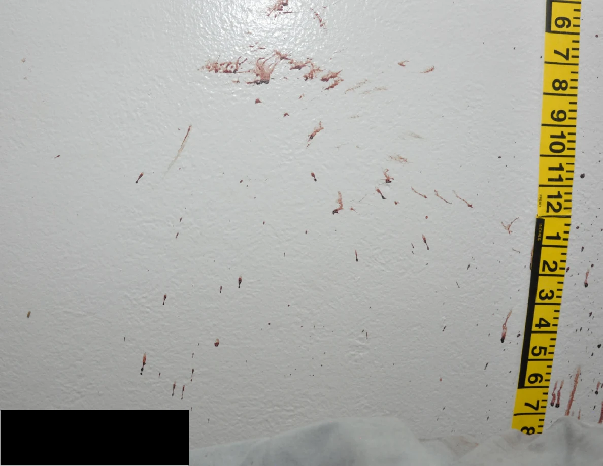 Reddish wall smears beside measuring tape above a black redaction.