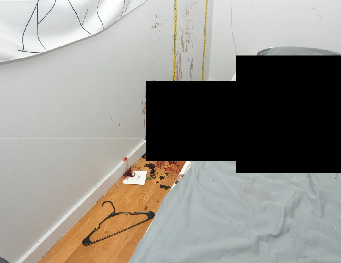 Clothes hanger on wood floor beside a bed, reddish wall streaks and black redactions.