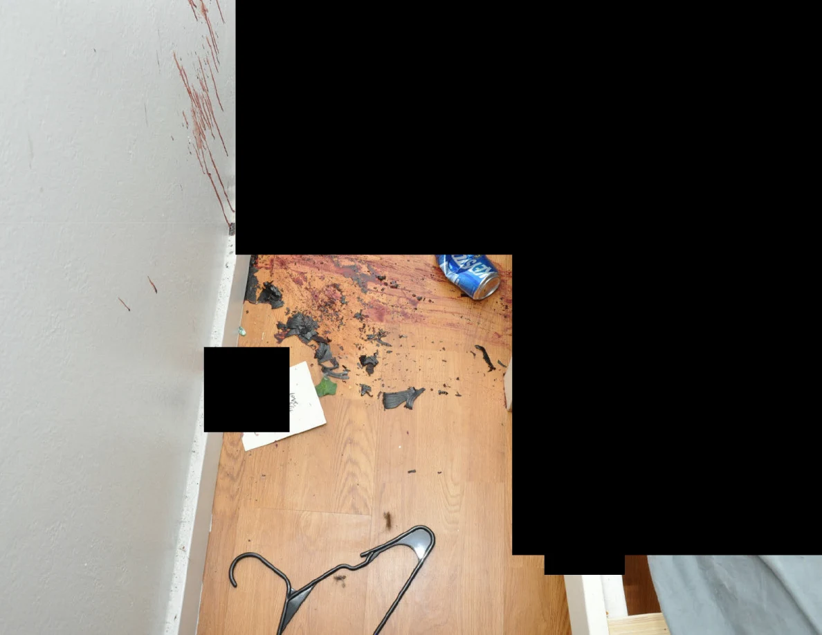 Clothes hanger and scattered fragments on wood floor below reddish wall marks and black redactions.