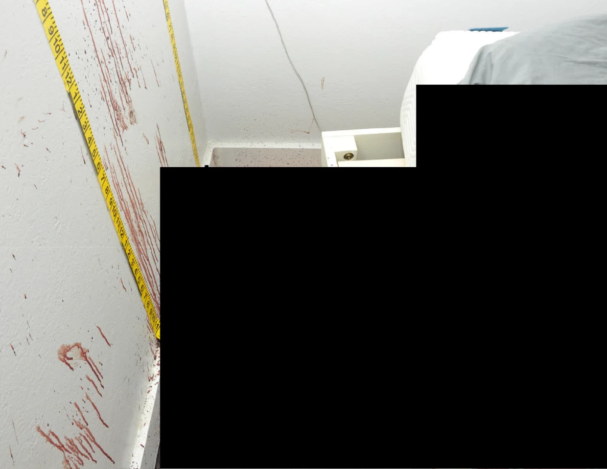 Reddish wall streaks beside measuring tape and a bed, with a large black redaction.