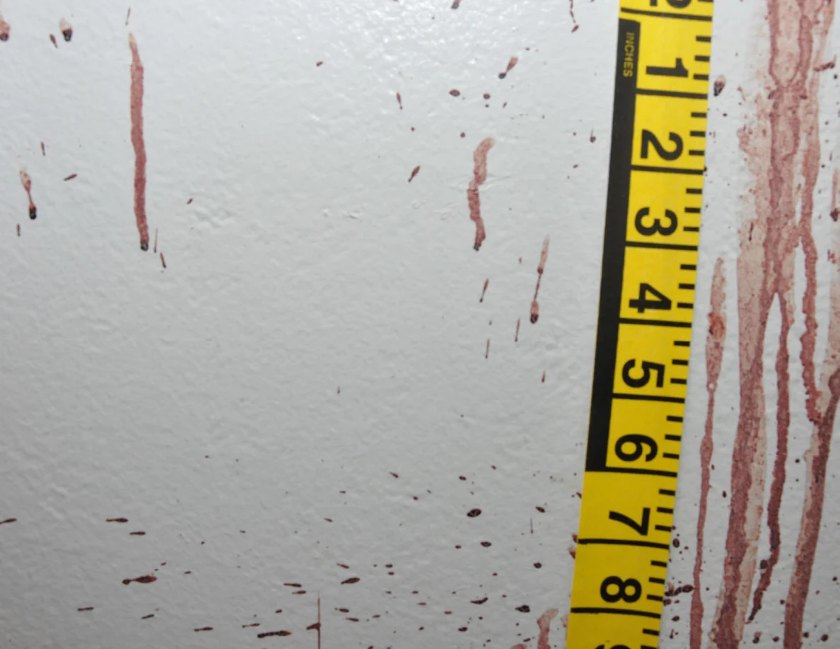 Reddish wall streaks and spots beside vertical yellow measuring tape.