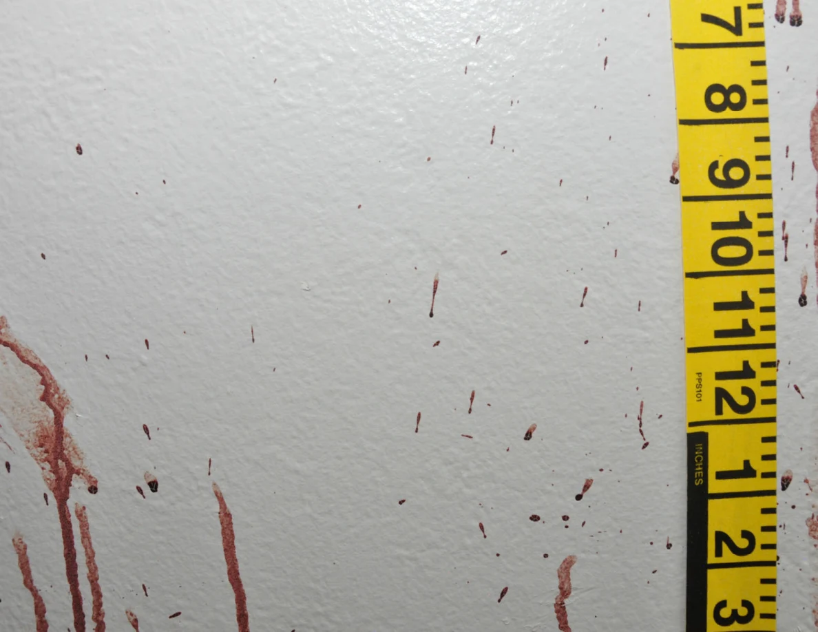 Reddish wall streaks and scattered spots beside vertical yellow measuring tape.
