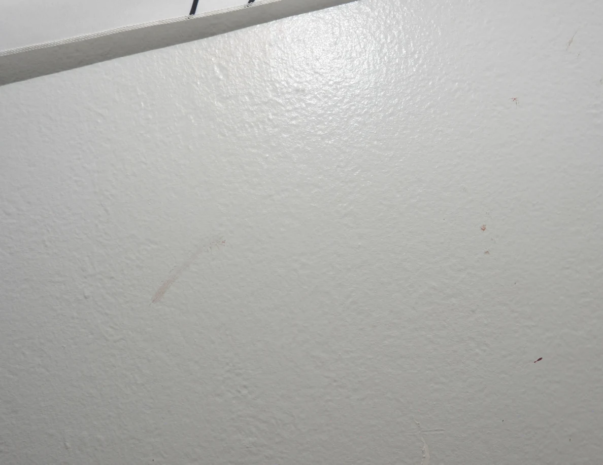 Faint diagonal mark on a white wall below a fabric hanging edge.
