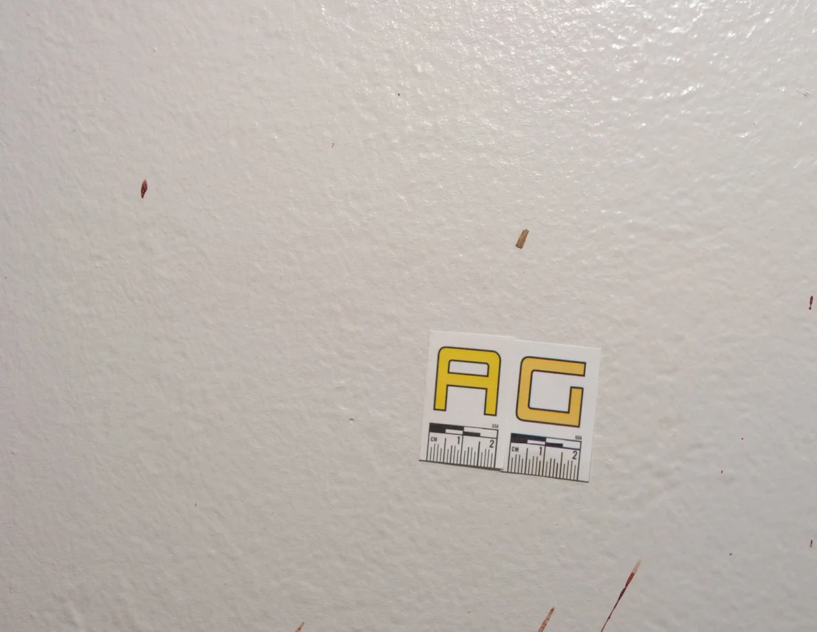 Close view of label AG on a white wall with scattered small spots.