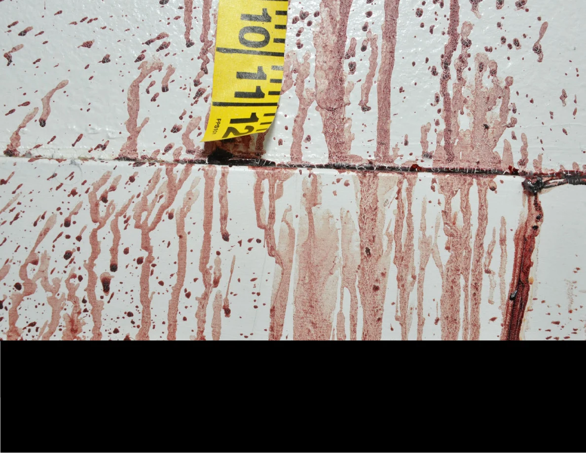 Reddish wall and baseboard streaks beside measuring tape above a black redaction.