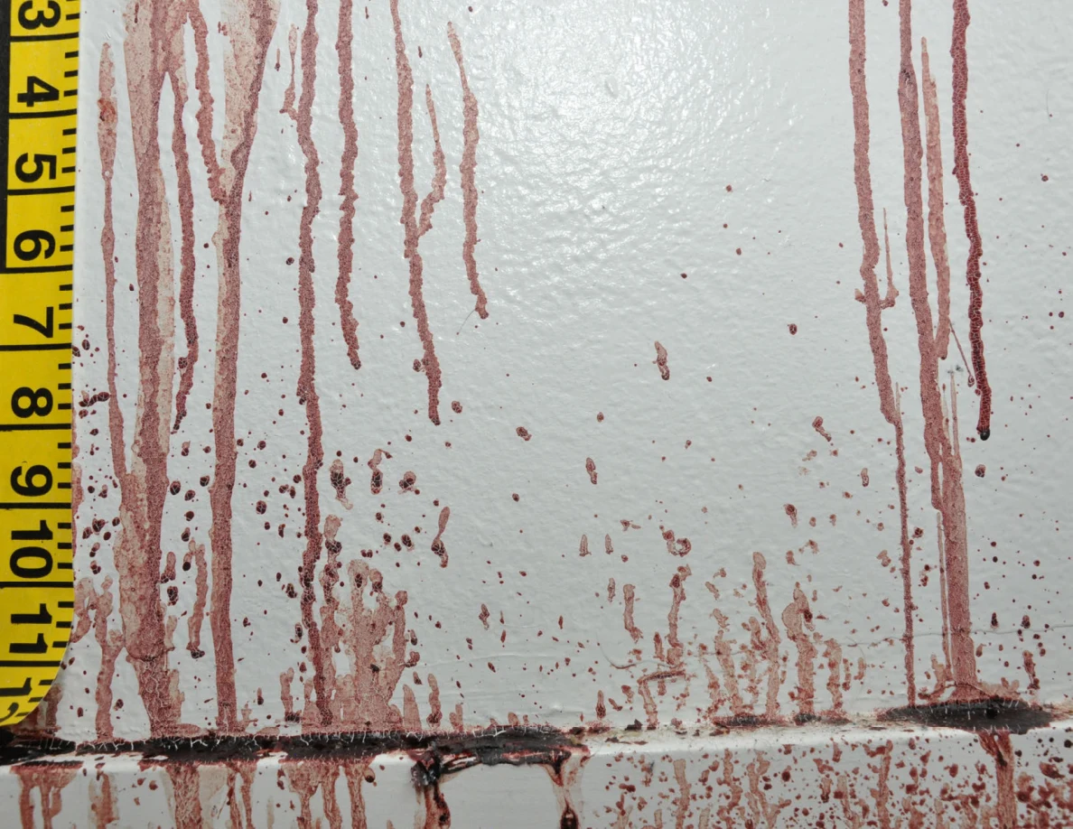 Reddish streaks extending down a white wall toward a baseboard beside measuring tape.