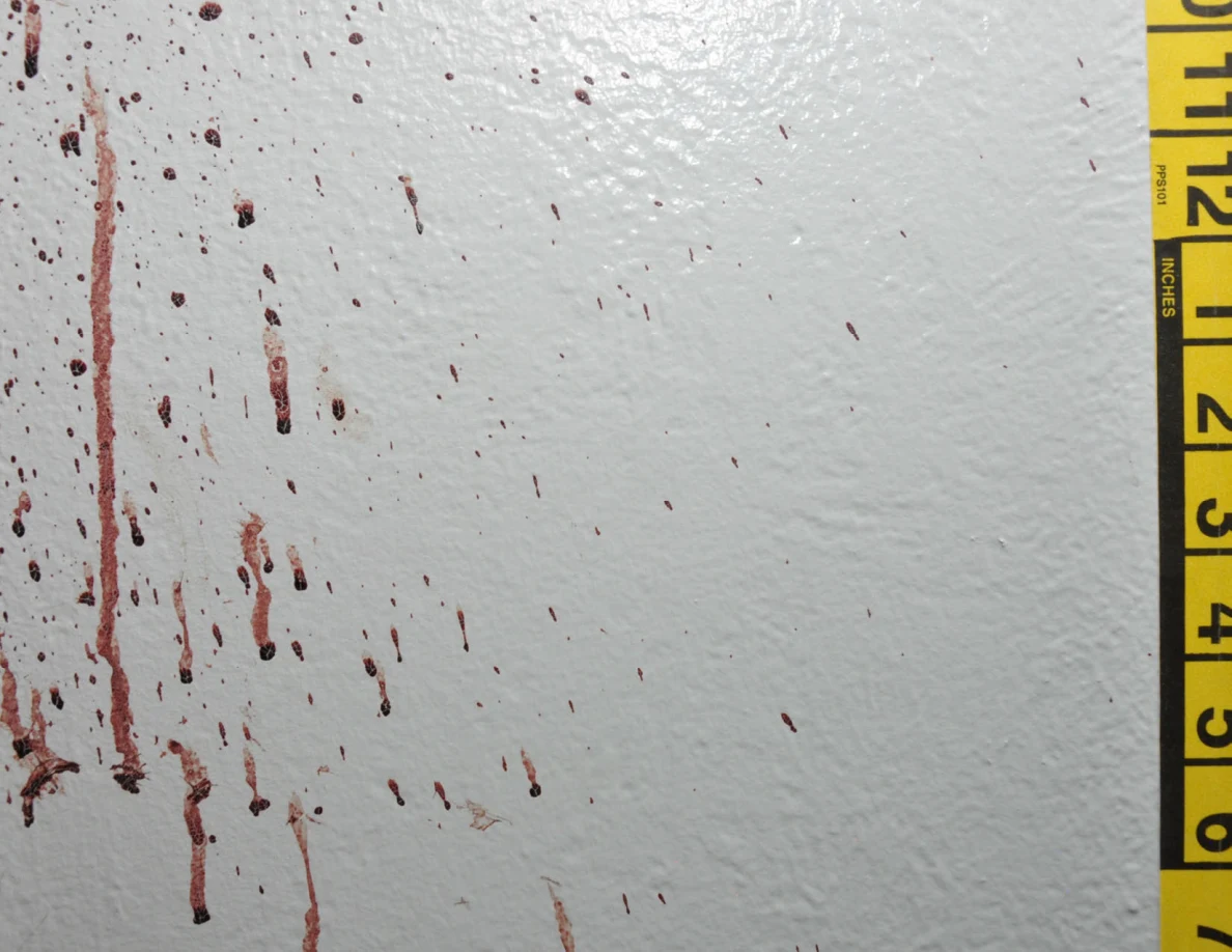 Reddish wall drops and streaks beside yellow measuring tape.