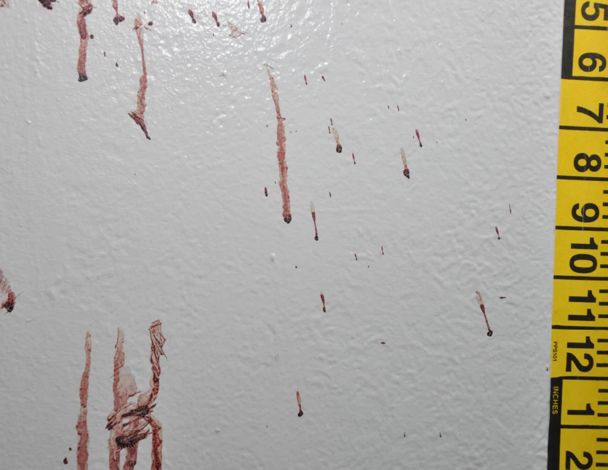Reddish wall streaks and a dark crossing mark beside yellow measuring tape.