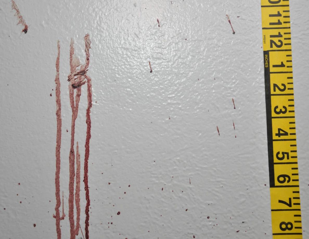 Long reddish wall streaks with a dark crossing mark beside measuring tape.
