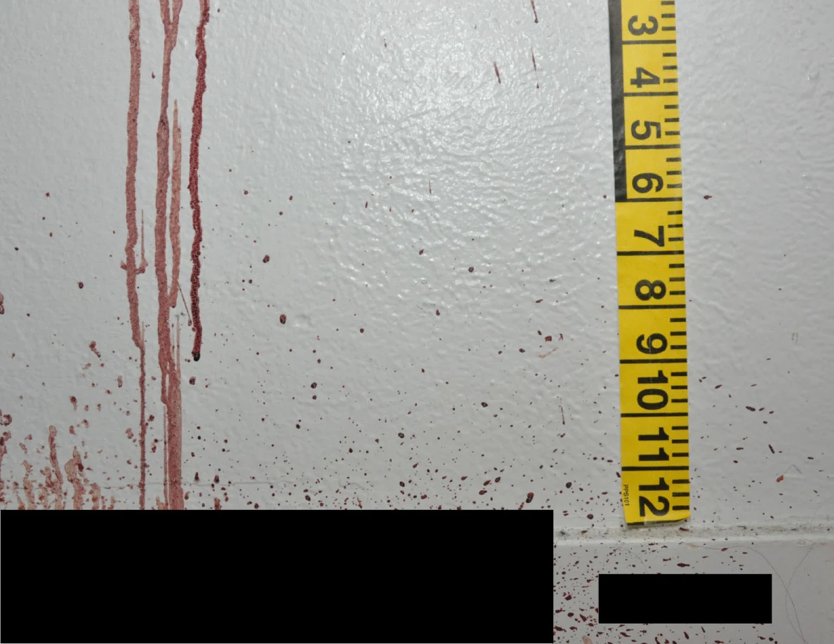 Reddish wall streaks beside measuring tape above black redactions.