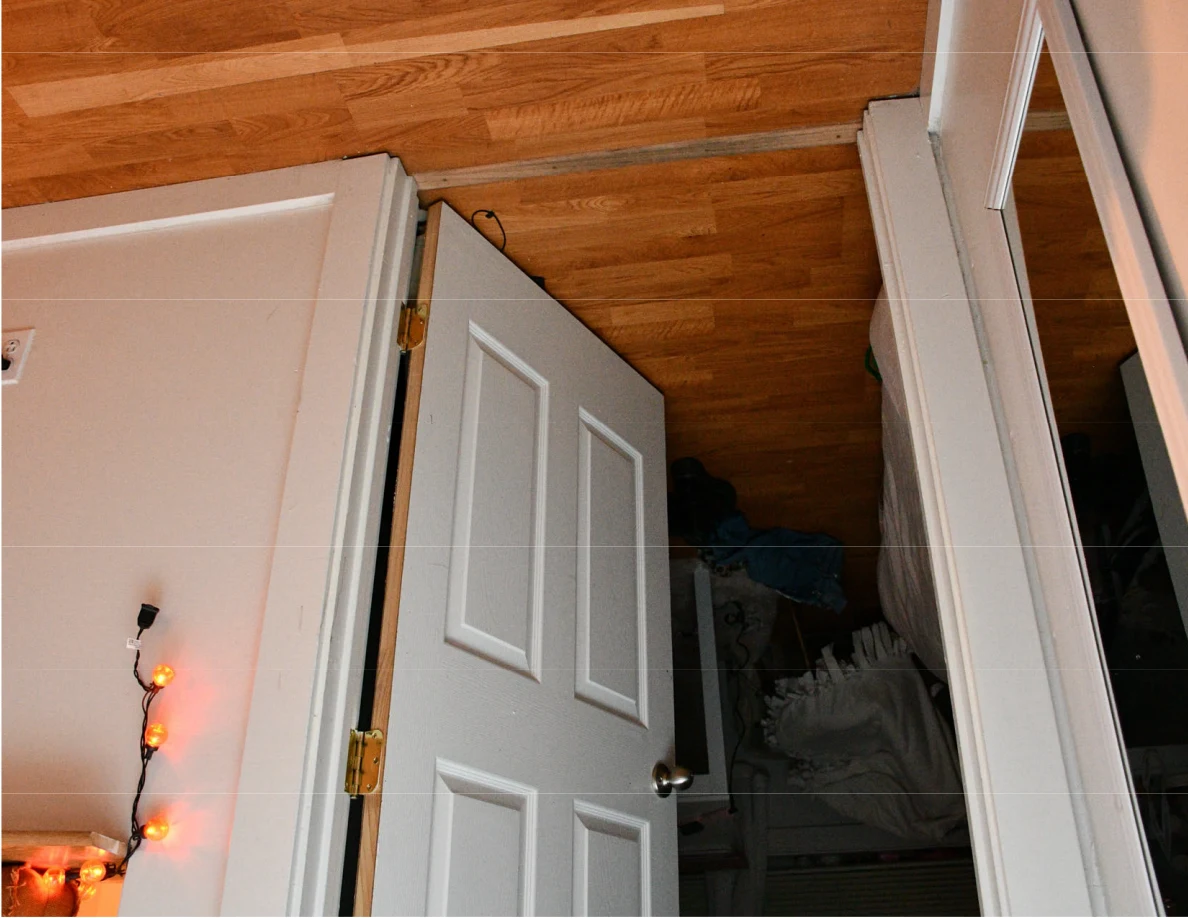 Tilted view of an open white door, wood flooring, mirror edge and string lights.