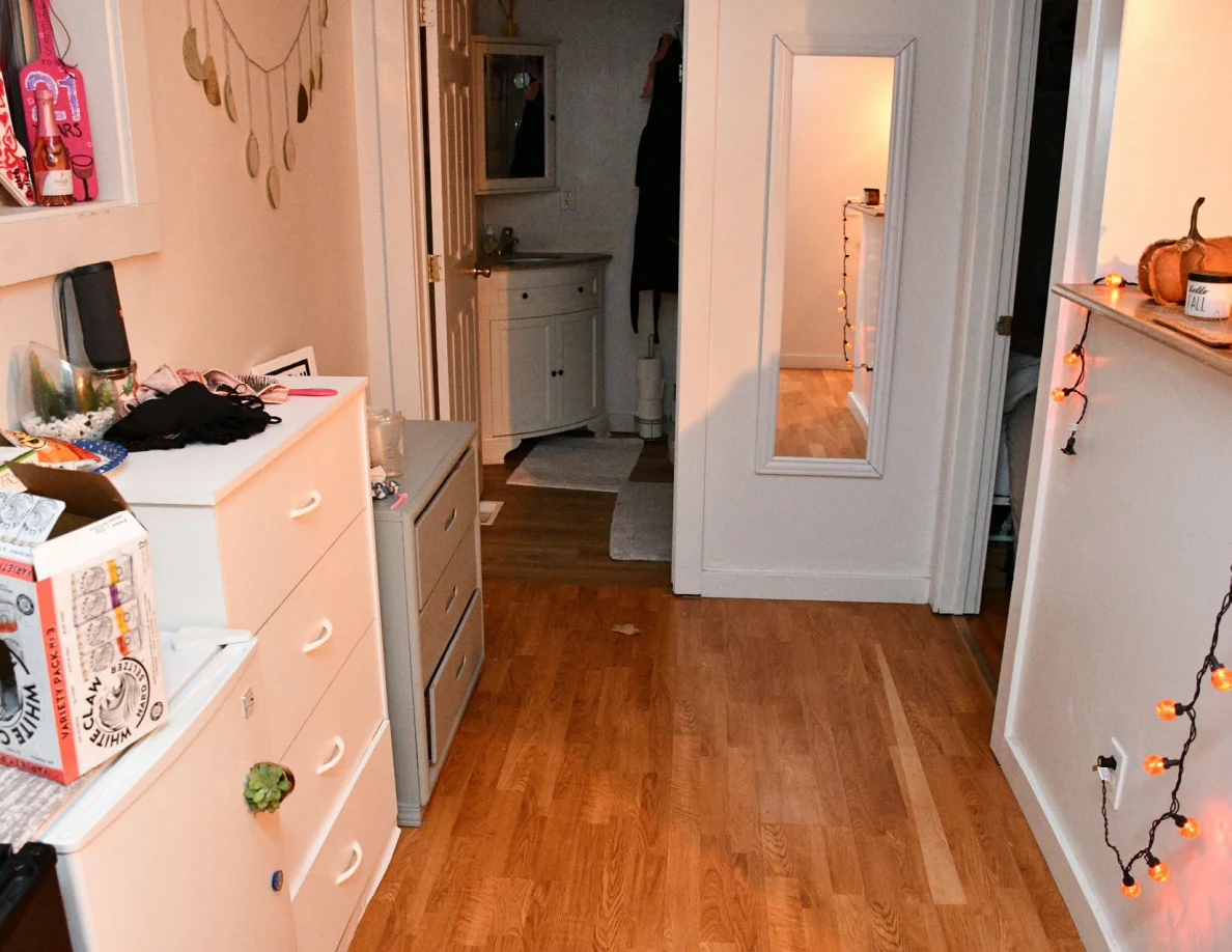 Hallway with white drawers, wall mirror, wood flooring and an open bathroom doorway.