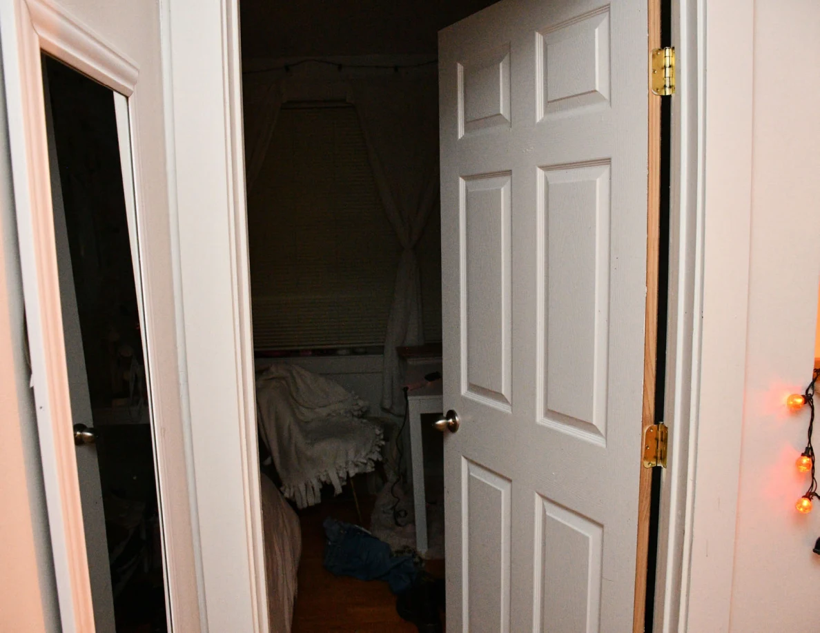Open white bedroom door with a bed and window visible inside.