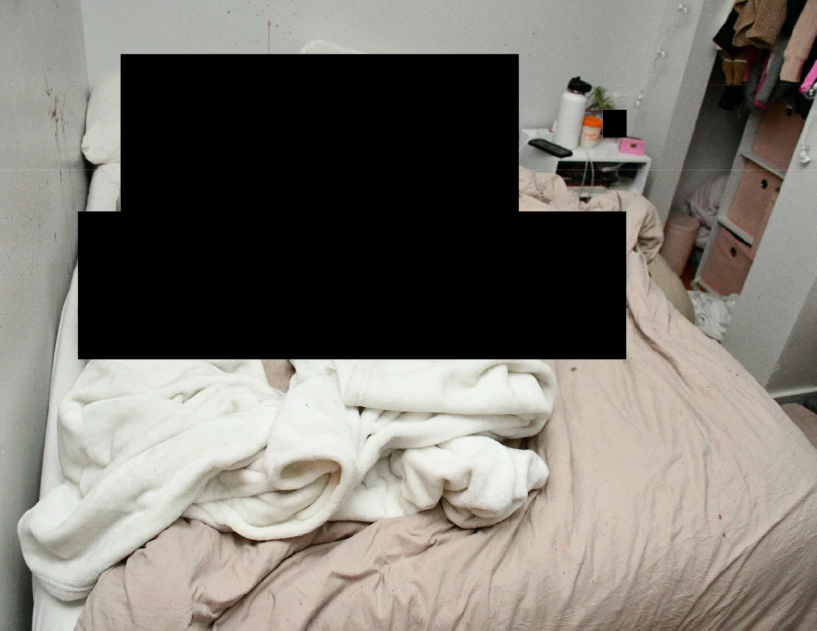 Rumpled bedding beside a small table and open closet, with large black redactions.