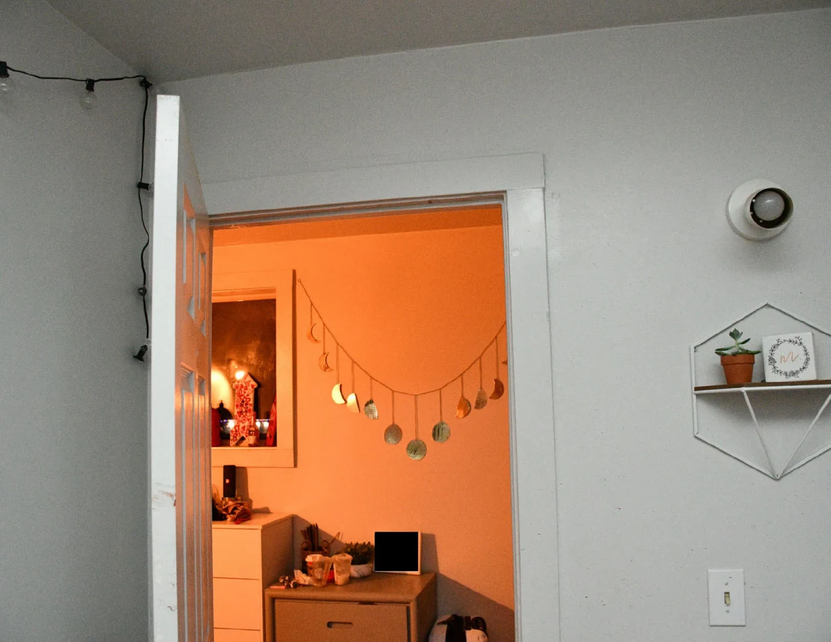 Open bedroom doorway looking into a warmly lit hall with drawers and hanging decorations.