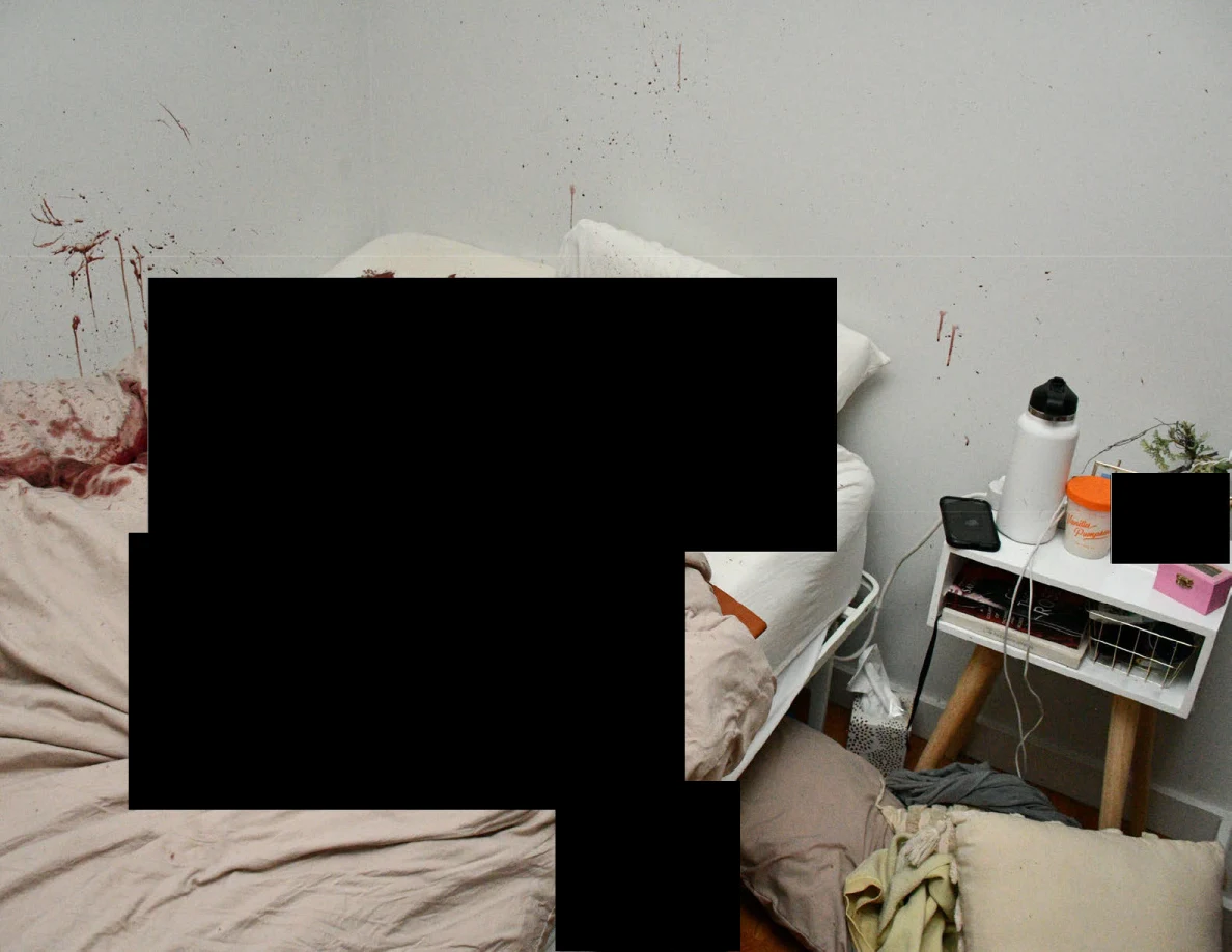 Bedside table with bottle and small objects beside reddish wall marks and black redactions.