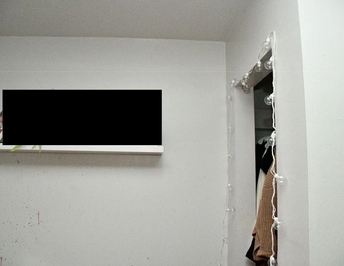 Bedroom wall and open closet edged with string lights, with a black redaction over a wall shelf.