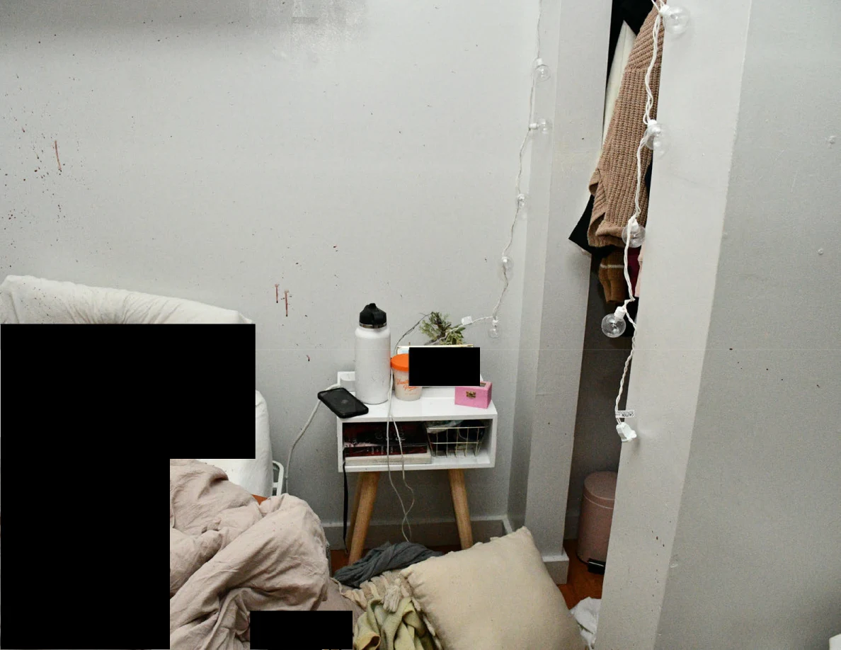 Small bedside table beside an open clothes closet, bedding and black redactions.