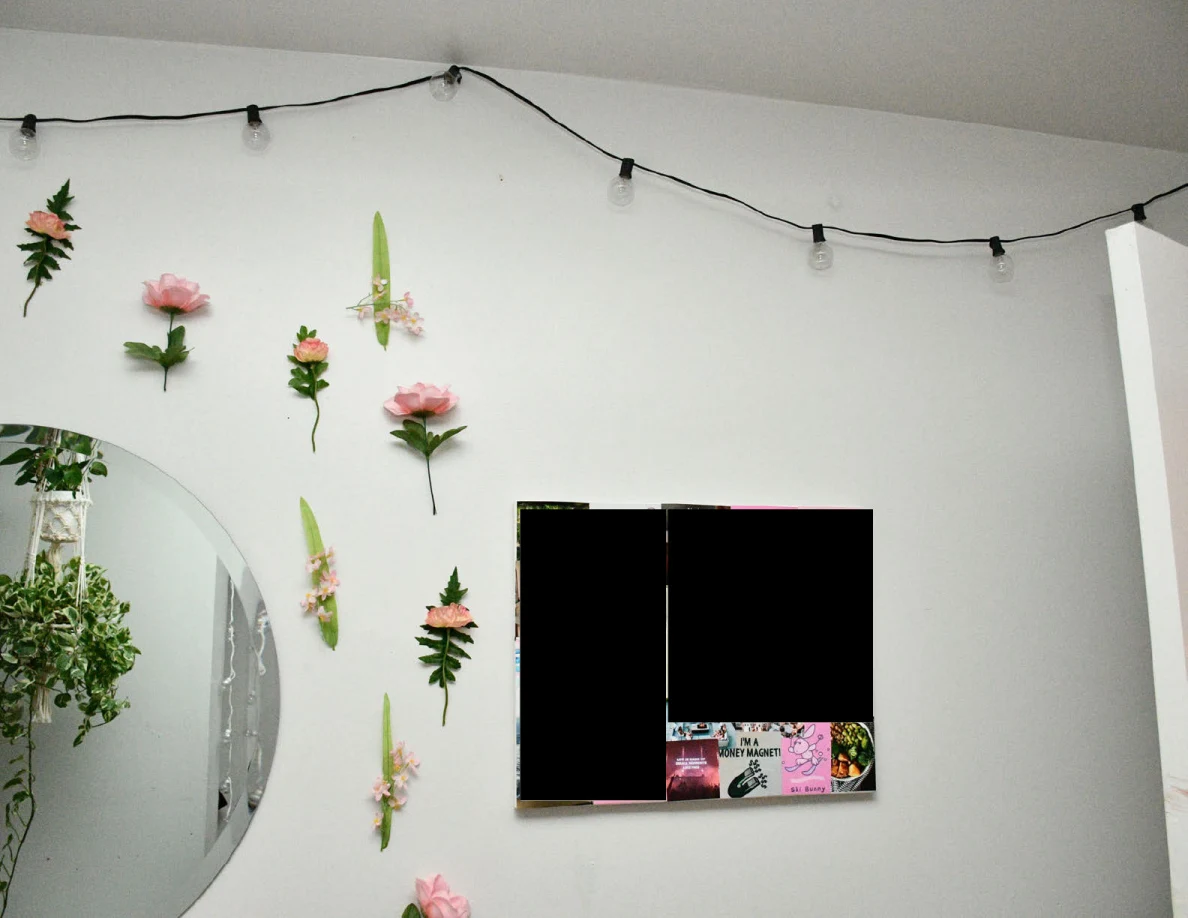 Artificial flowers, round mirror and string lights on bedroom wall beside redacted wall art.