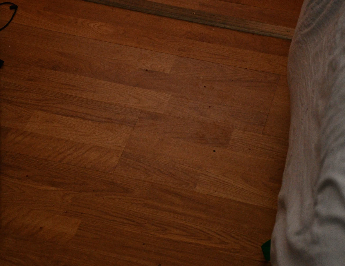 Close view of wood flooring beside the edge of a bed.