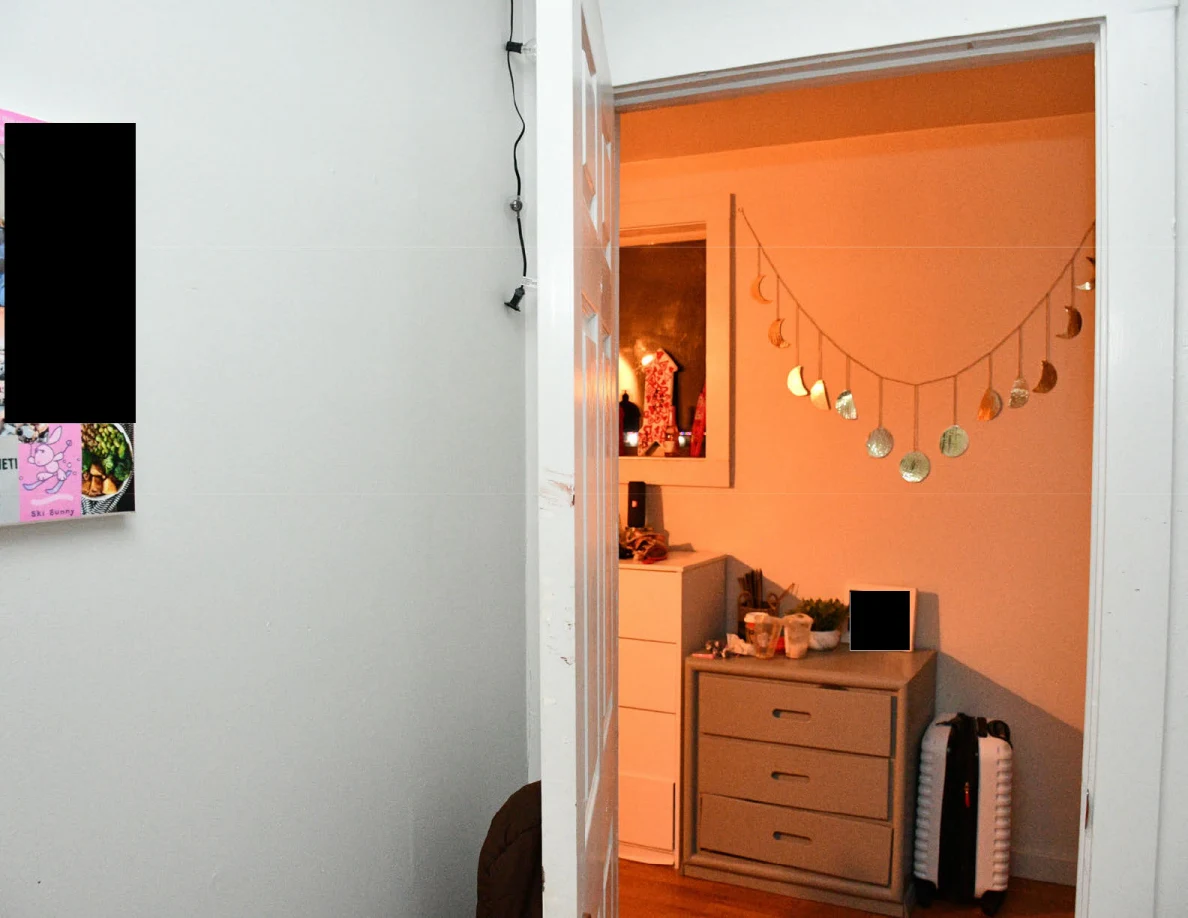 Open bedroom doorway looking toward drawers, suitcase and hanging decorations in a warmly lit hall.