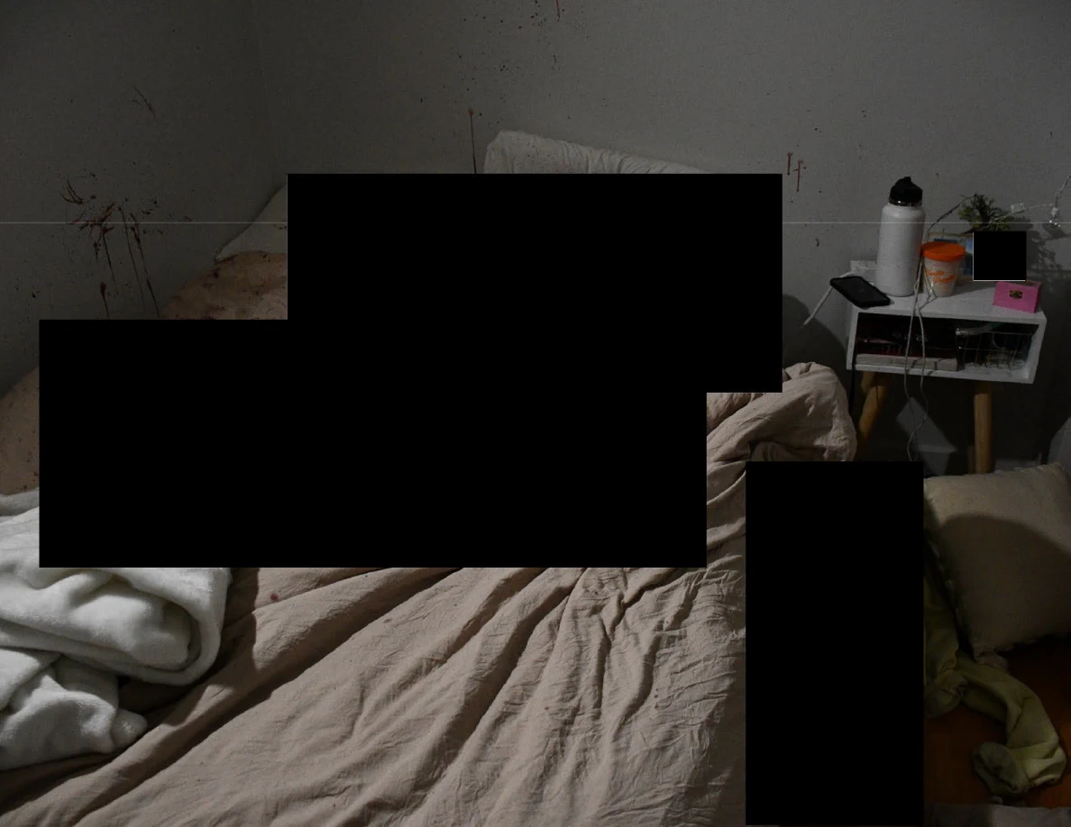 Dim view of bedding and bedside table around large black redactions.