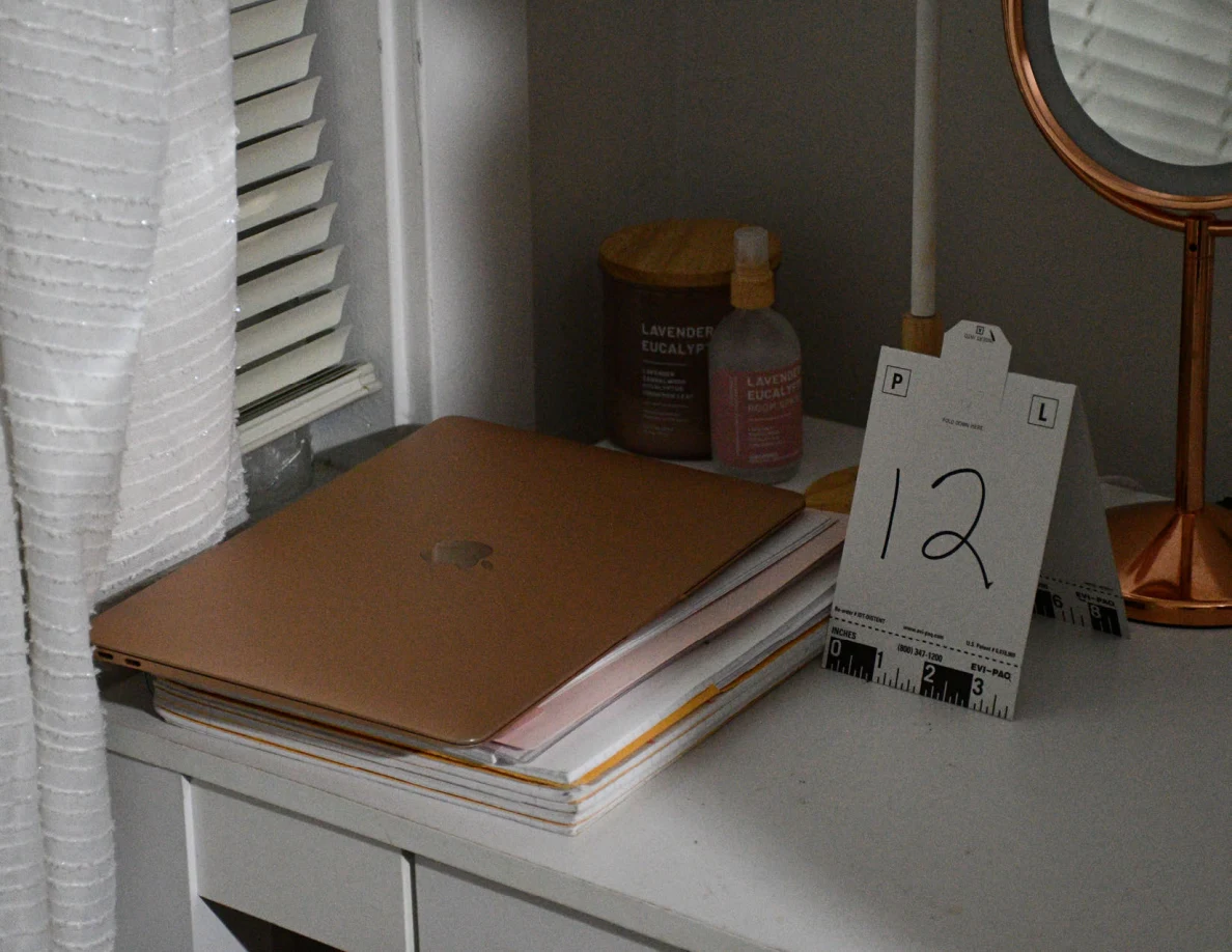 Closed laptop on stacked papers beside candle, spray bottle and evidence marker 12.