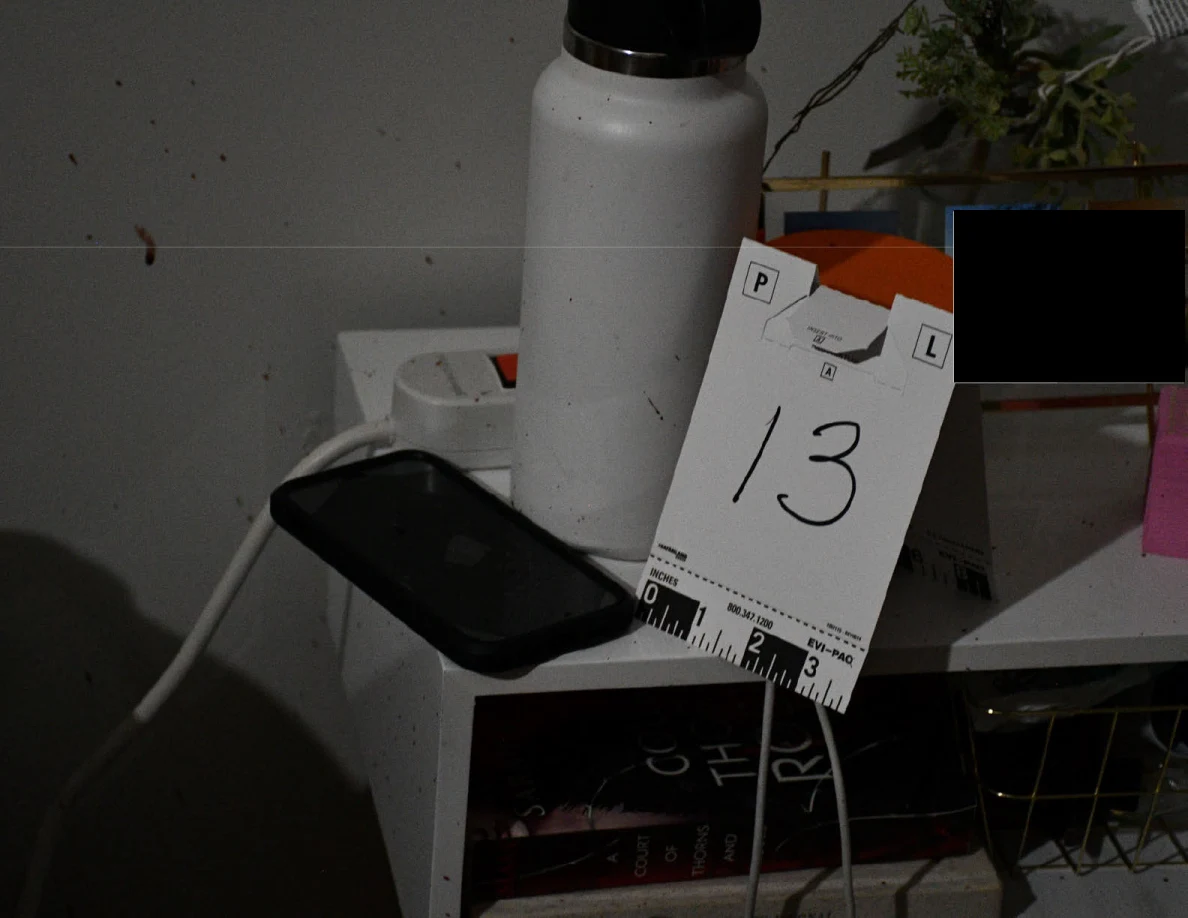 Black phone and white bottle beside evidence marker 13 on bedside table.