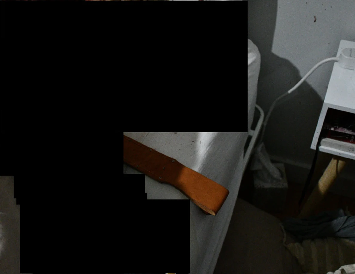 Brown leather sheath along a white mattress edge beside a bedside table, with black redactions.