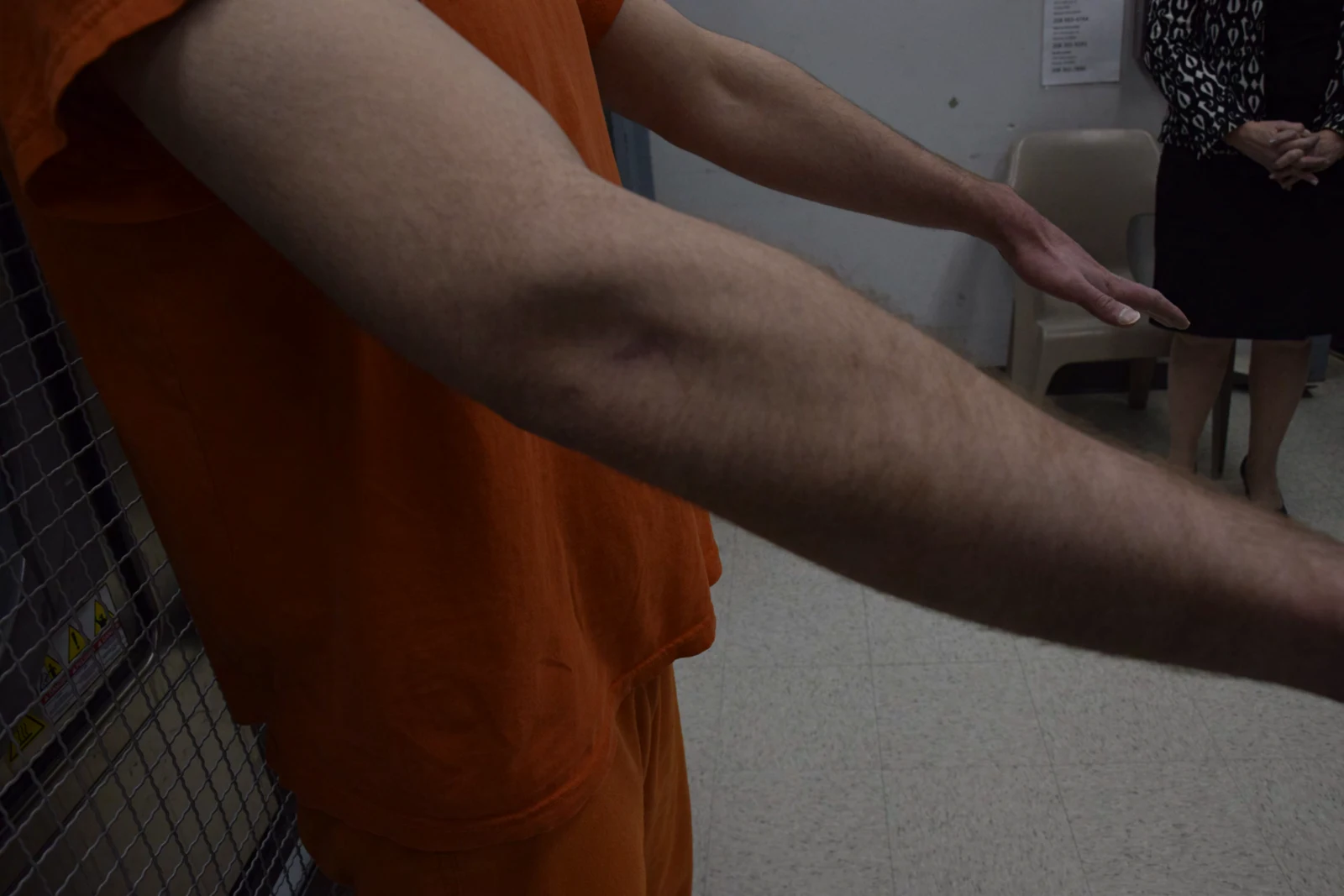 Oblique view of both outstretched arms and hands above a light-colored floor, beside orange clothing.