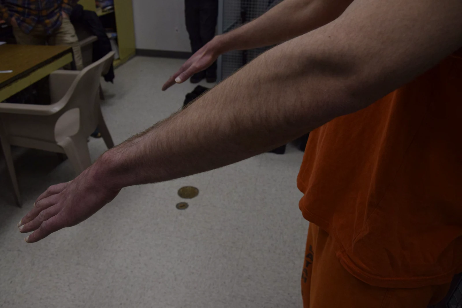 Side view of two outstretched forearms and hands with fingers extended above a light-colored floor.