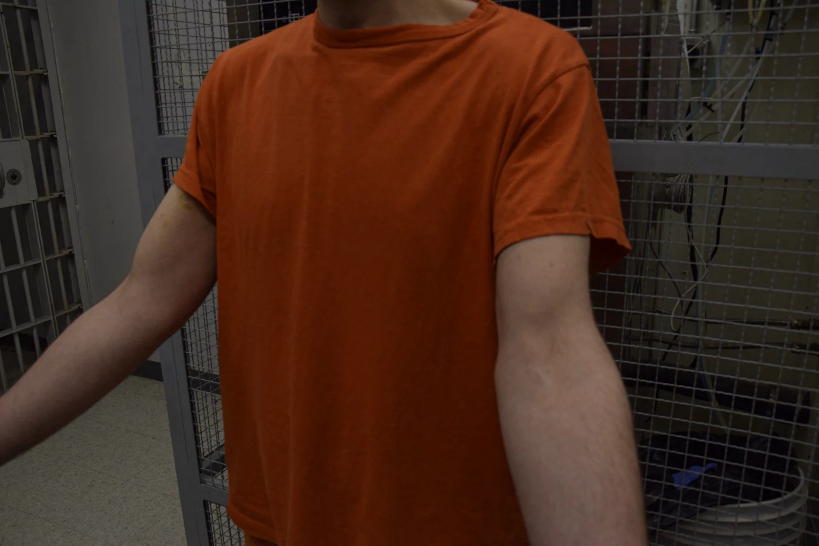 Wider torso view of a person in orange clothing holding both arms forward, with the face cropped above the mouth.