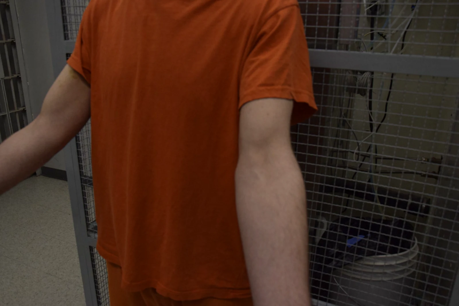 Angled view of an orange-shirted torso and extended bare arm, with a gray mesh enclosure behind.