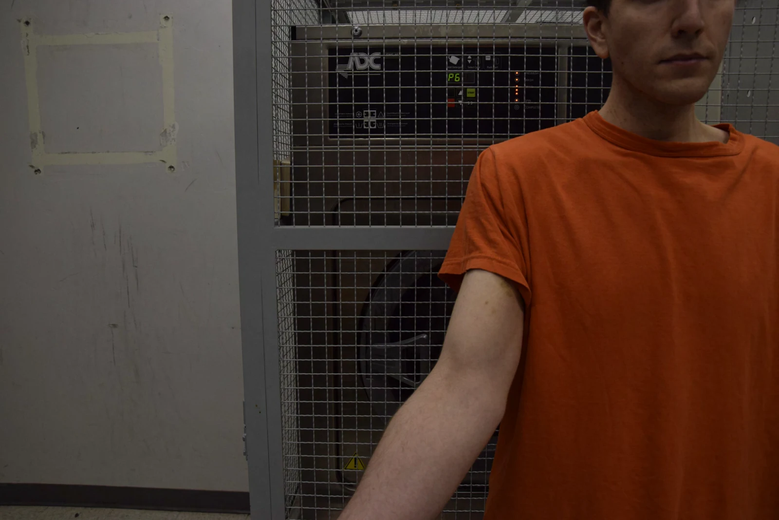 Upper-body view of a person in an orange shirt holding an arm forward; part of the face is visible near the top edge.